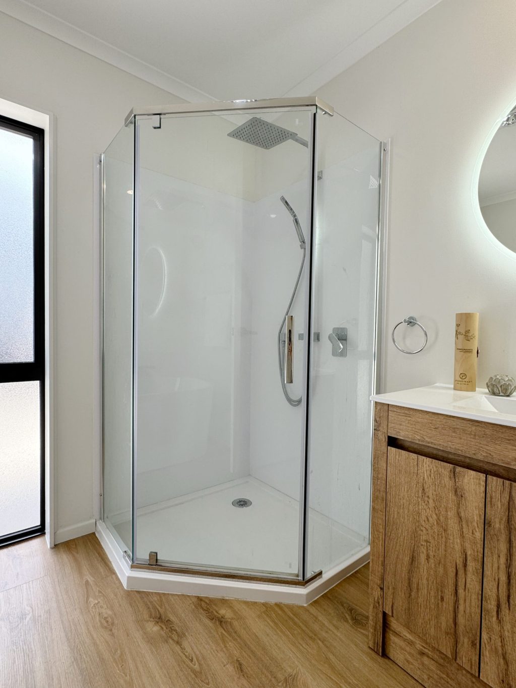 Glass shower enclosure with wooden vanity in modern bathroom.