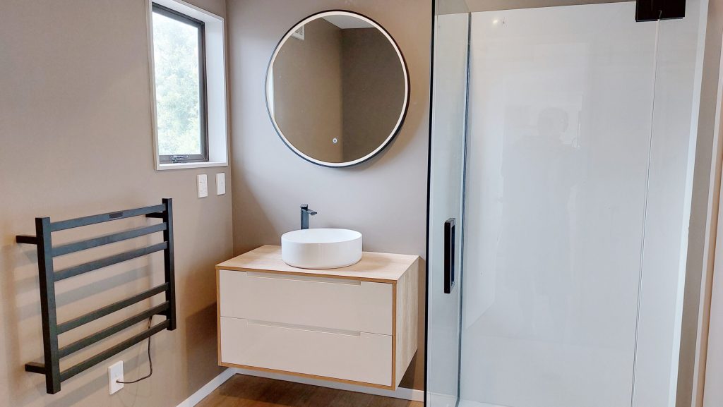 Modern bathroom with round mirror, vessel sink, and glass shower door.