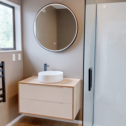 Modern bathroom with round mirror, vessel sink, and glass shower door.
