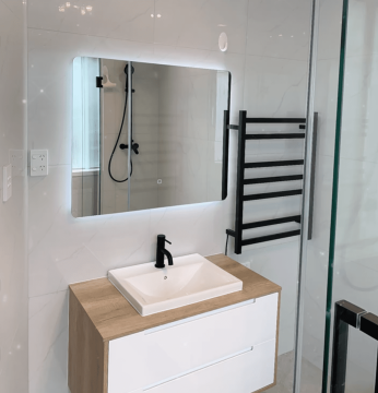 Modern bathroom with illuminated mirror, sink, and black towel rack.
