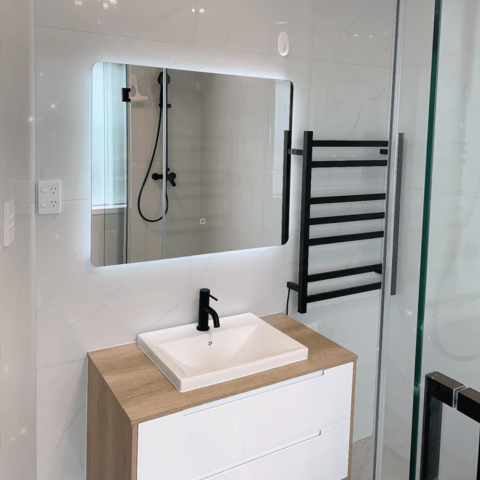 Modern bathroom with illuminated mirror, sink, and black towel rack.