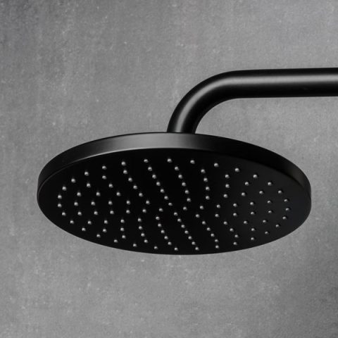 Black round showerhead against a gray wall.