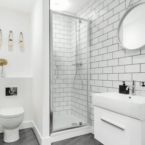 Modern bathroom with shower, white tiles, round mirror, and sink.