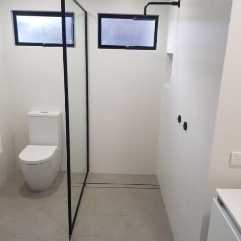 Minimalist bathroom with glass shower partition and modern toilet.