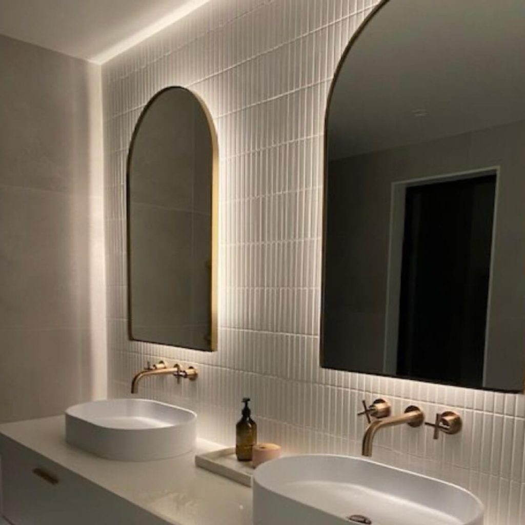 Modern bathroom with two sinks, arched mirrors, and gold fixtures.