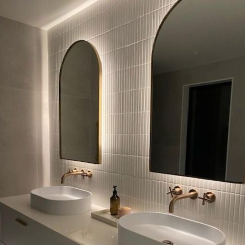 Modern bathroom with two sinks, arched mirrors, and gold fixtures.