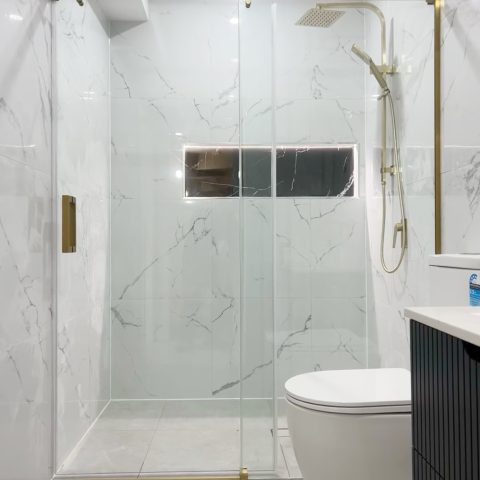 Modern bathroom with glass shower, marble walls, and gold fixtures.