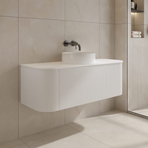 Modern white bathroom sink with wall-mounted faucet and beige tiled walls.