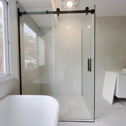 Modern bathroom with glass shower enclosure and white bathtub.