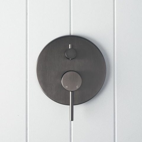 Round matte black shower control on white paneled wall.