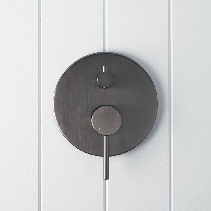 Round matte black shower control on white paneled wall.