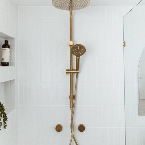 Gold shower fixture against white tiled wall in modern bathroom.