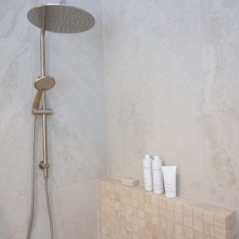 Shower with beige tiles and toiletries on ledge.