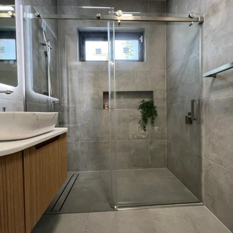 Modern bathroom with glass shower door and wooden vanity.