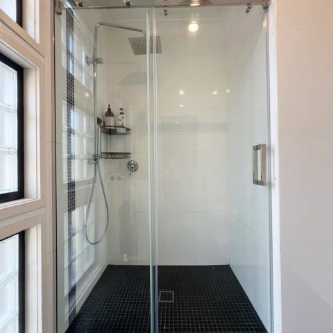 Modern glass shower with black tile floor and wall-mounted showerhead.