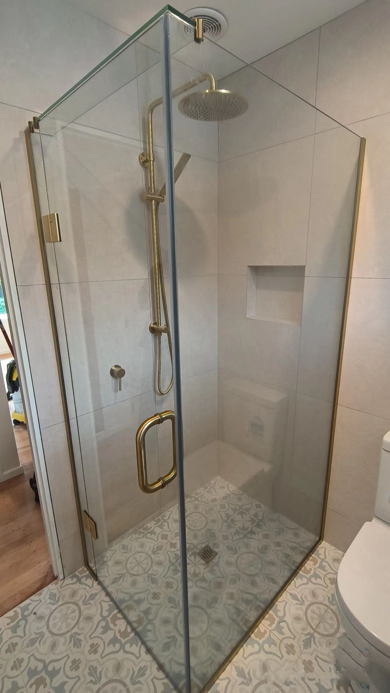 Modern shower with glass door, gold fixtures, and built-in shelf.