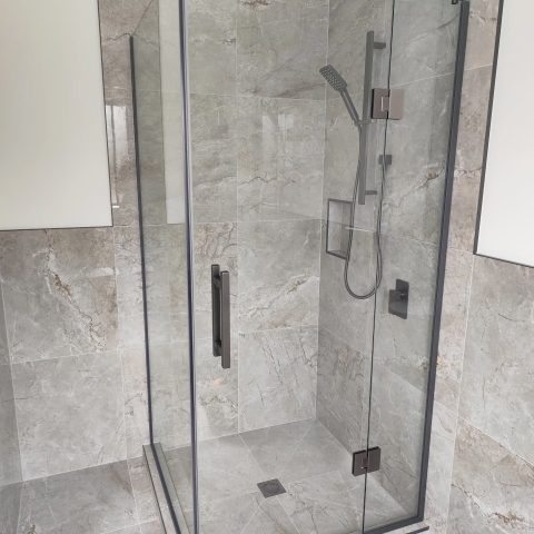 Glass shower enclosure with marble walls and modern fixtures.