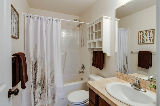Small bathroom with a shower curtain featuring botanical design, wooden vanity, and light-toned tile accents.