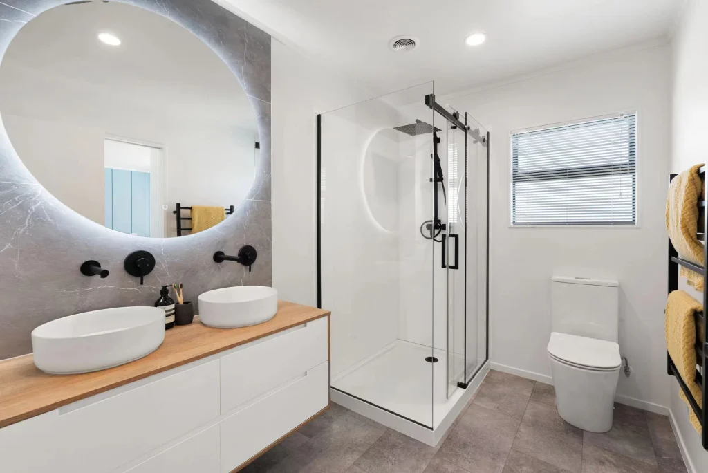 Modern bathroom with double vanity, LED backlit mirror, glass shower box, and sleek floor tiles
